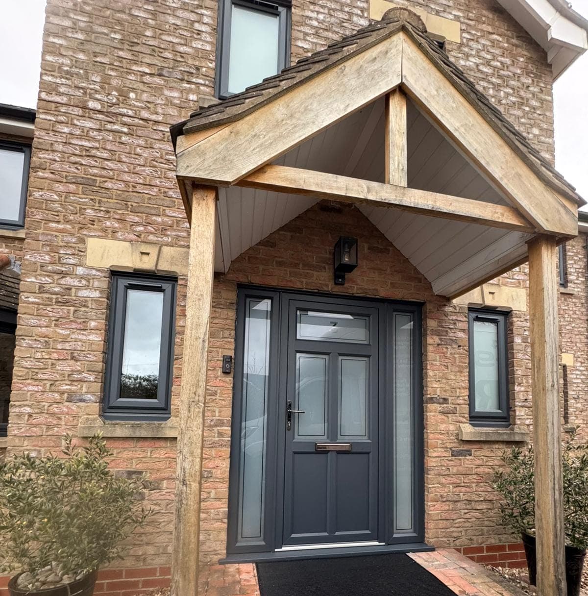 Anthracite grey front door with frosted glass side panels under an oak framed porch