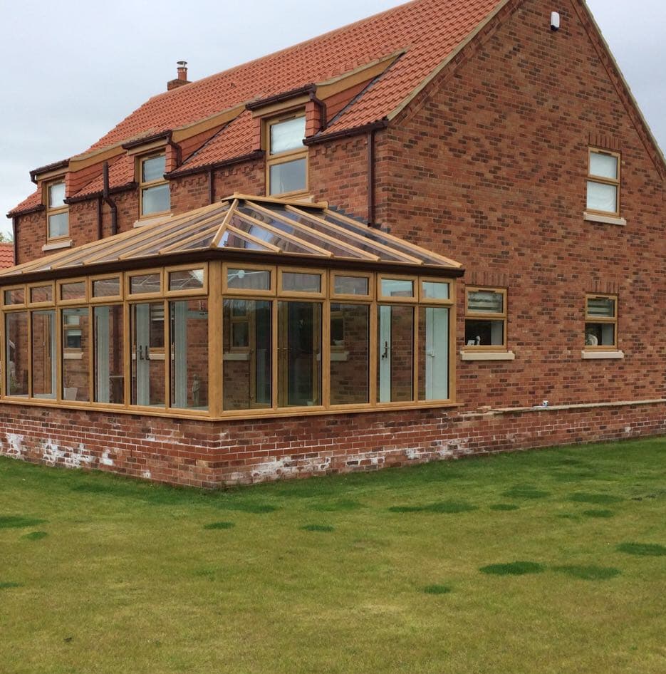 Golden oak effect conservatory with a hipped glazed roof beside a red brick house