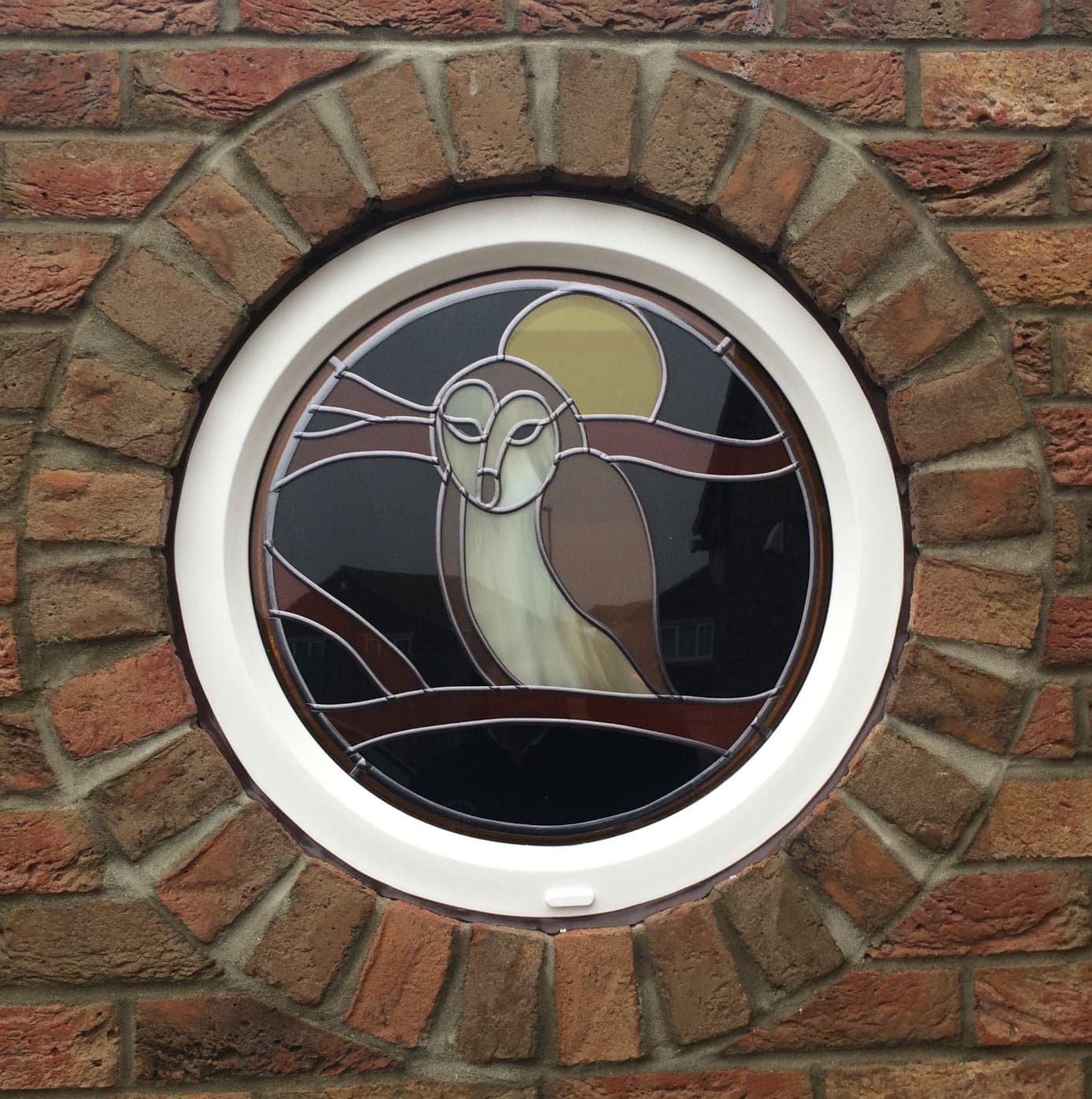 Round white uPVC window with a leaded stained glass owl and moon in a circular brick surround
