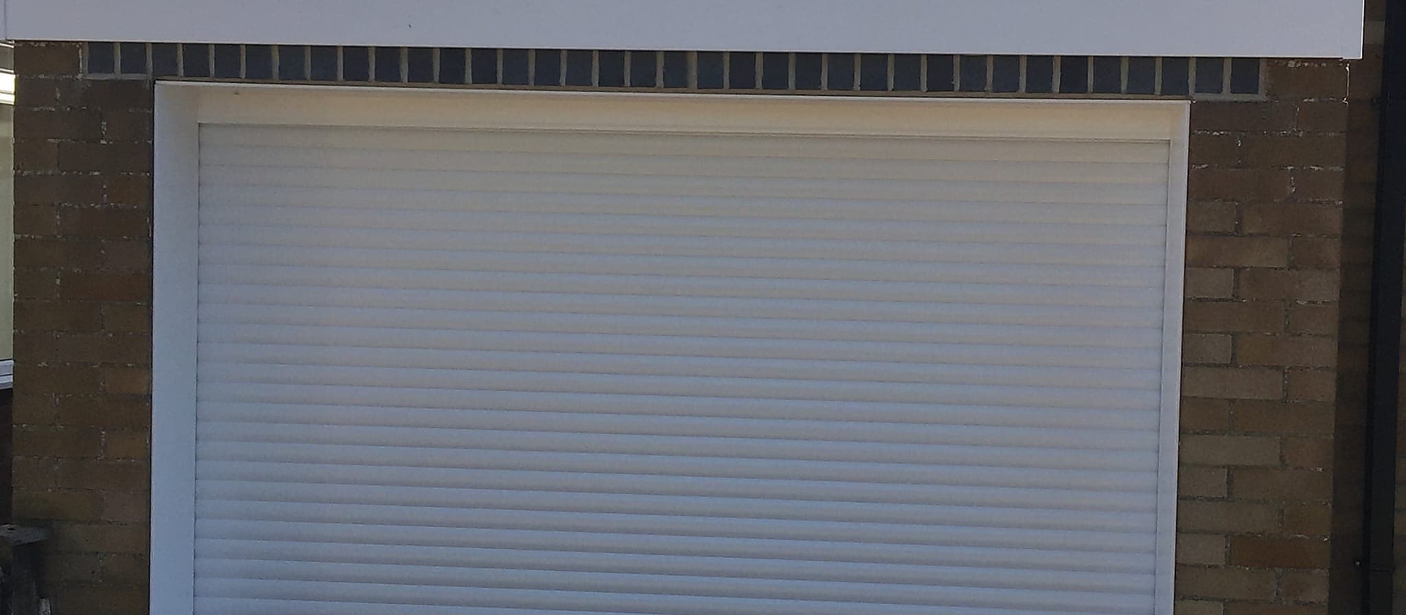 White roller garage door closed in its side guides on a flat roofed brick garage